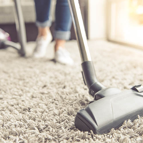 Cropped image of beautiful young woman using a vacuum cleaner while cleaning carpet in the house